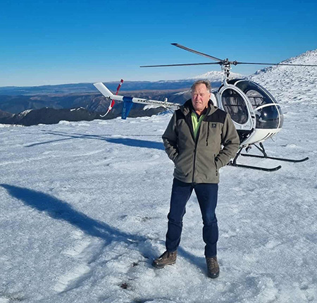 Rick standing in snow in front of his helicopter.