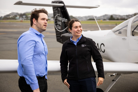 Man and woman standing beside fixed wing aircraft.