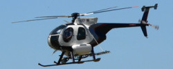 Hughes 369D helicopter in air above trees
